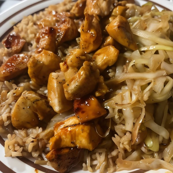 Hibachi chicken with brown rice and sautéed cabbage, glistening with sauce in a white bowl.