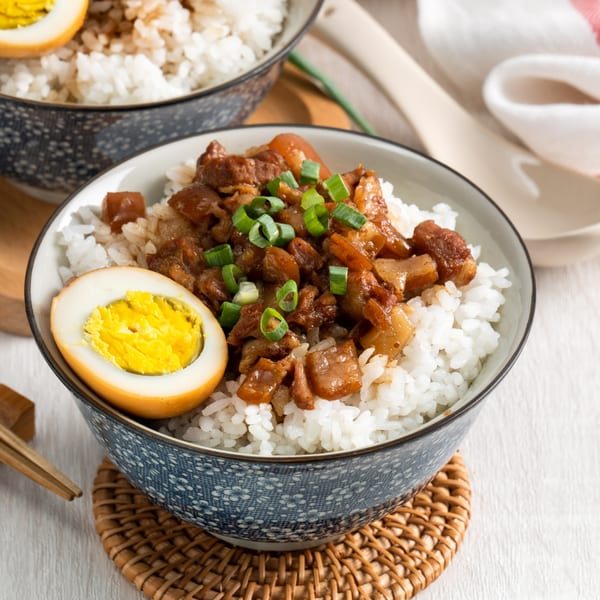 Two bowls of Japanese braised pork belly over rice, garnished with green onions and a hard-boiled egg.