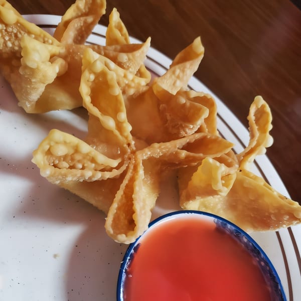 Crispy golden crab rangoons with a side of sweet red dipping sauce on a white plate.