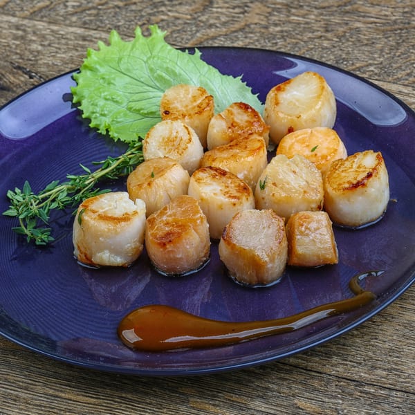 Seared scallops with fresh thyme, lettuce, and a drizzle of sauce on a blue plate.