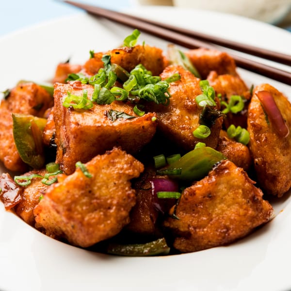 Close-up of Japanese fried tofu with green onions, bell peppers, and red onions in a white bowl.