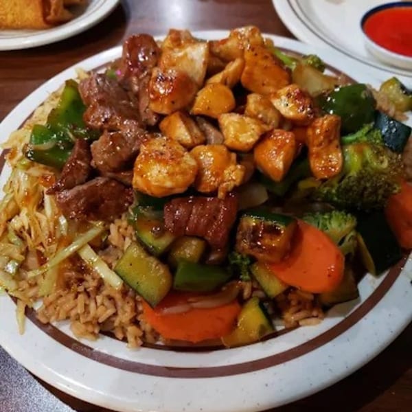 A hibachi dinner with chicken, steak, rice, and mixed vegetables on a white plate.